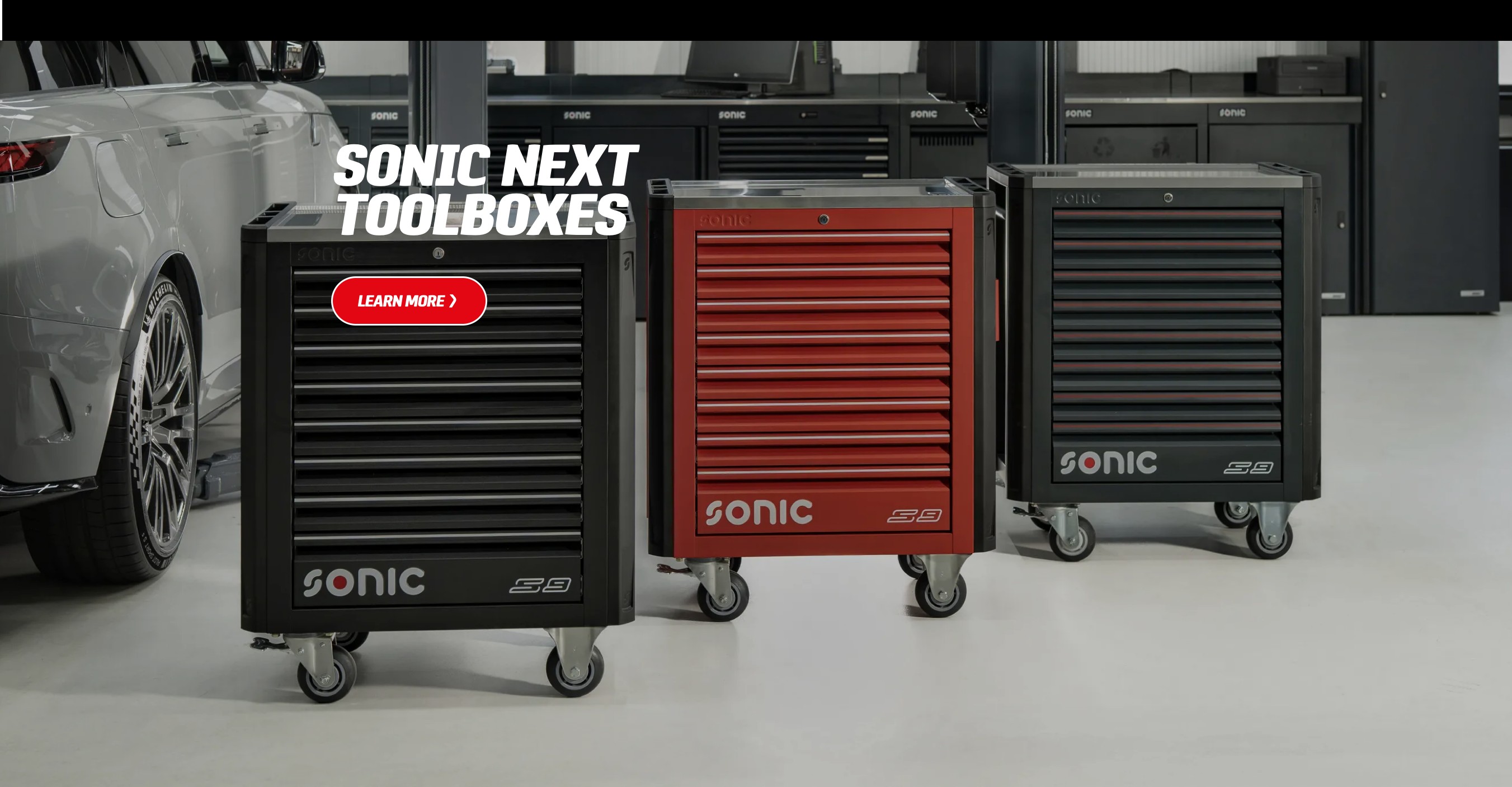 Dãy ba tủ đồ nghề Sonic NEXT (đen, đỏ, đen) trong xưởng cùng một chiếc xe